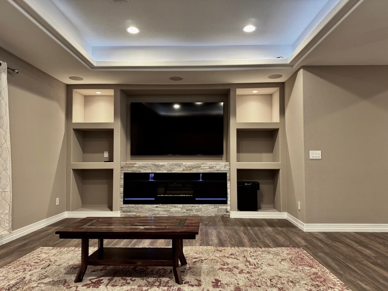 Finished basement media room with built-in shelving and stone fireplace by JH Basement Finish