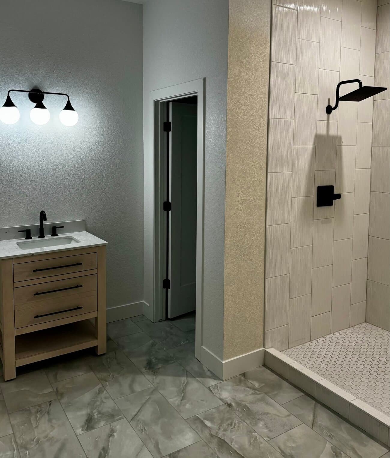 Modern basement bathroom with wood vanity, black fixtures and marble-look tile