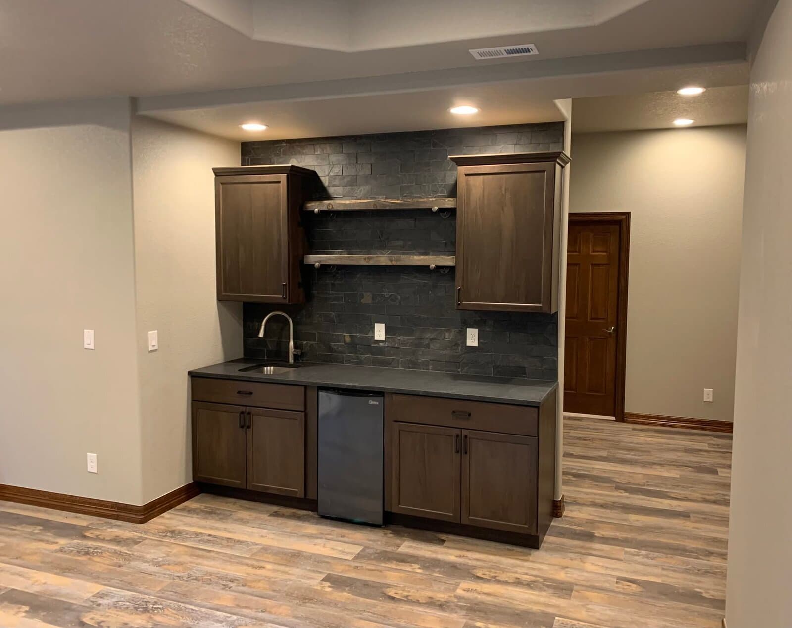 Wet bar with dark wood cabinetry and dark stone backsplash